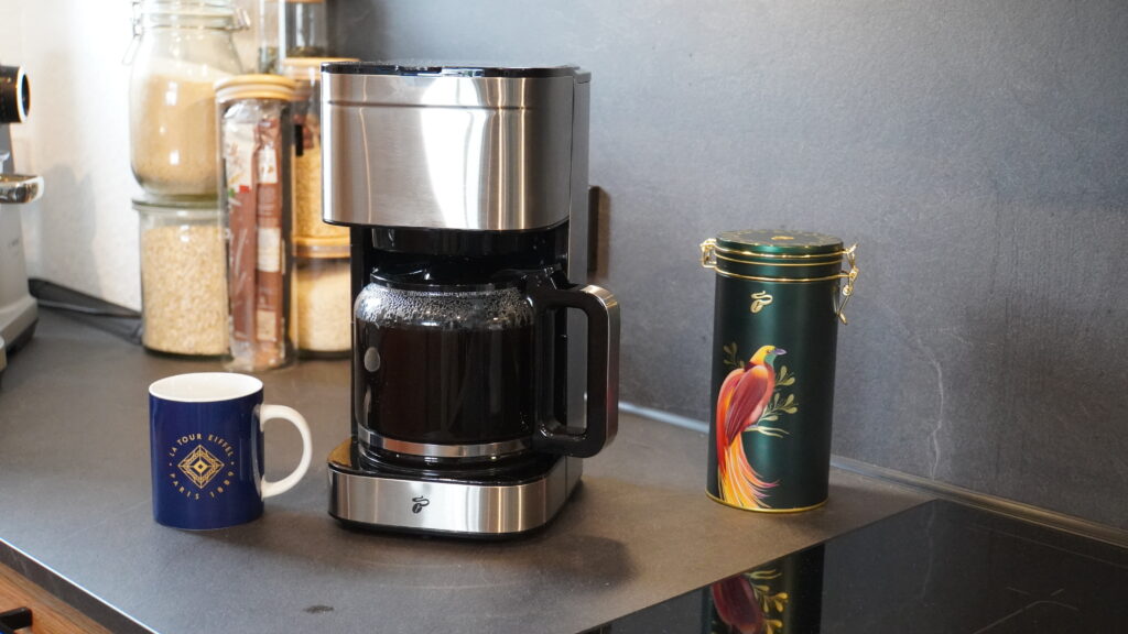 Kaffeemaschine mit schwarzer Kaffeekanne und blauer Tasse auf einer Arbeitsplatte.