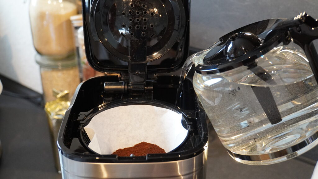 Kaffeemaschine Let’s Brew Elegant mit einem Filtereinsatz, in den Wasser gegossen wird, während gemahlener Kaffee sichtbar ist.